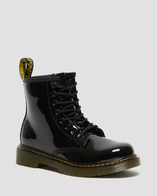A stock photo of a child's Dr Marten 1460 Patent leather boot with a full wrap-around zipper, displaying a black leather upper, a yellow pull tab, and a green sole.